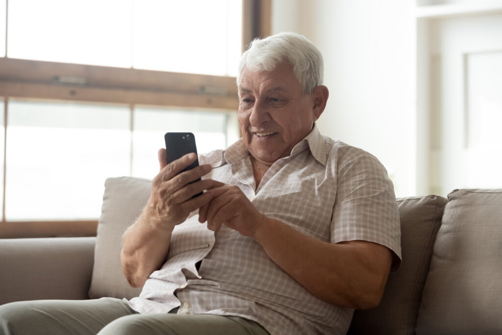 Older gentleman sits, smiling at a smartphone